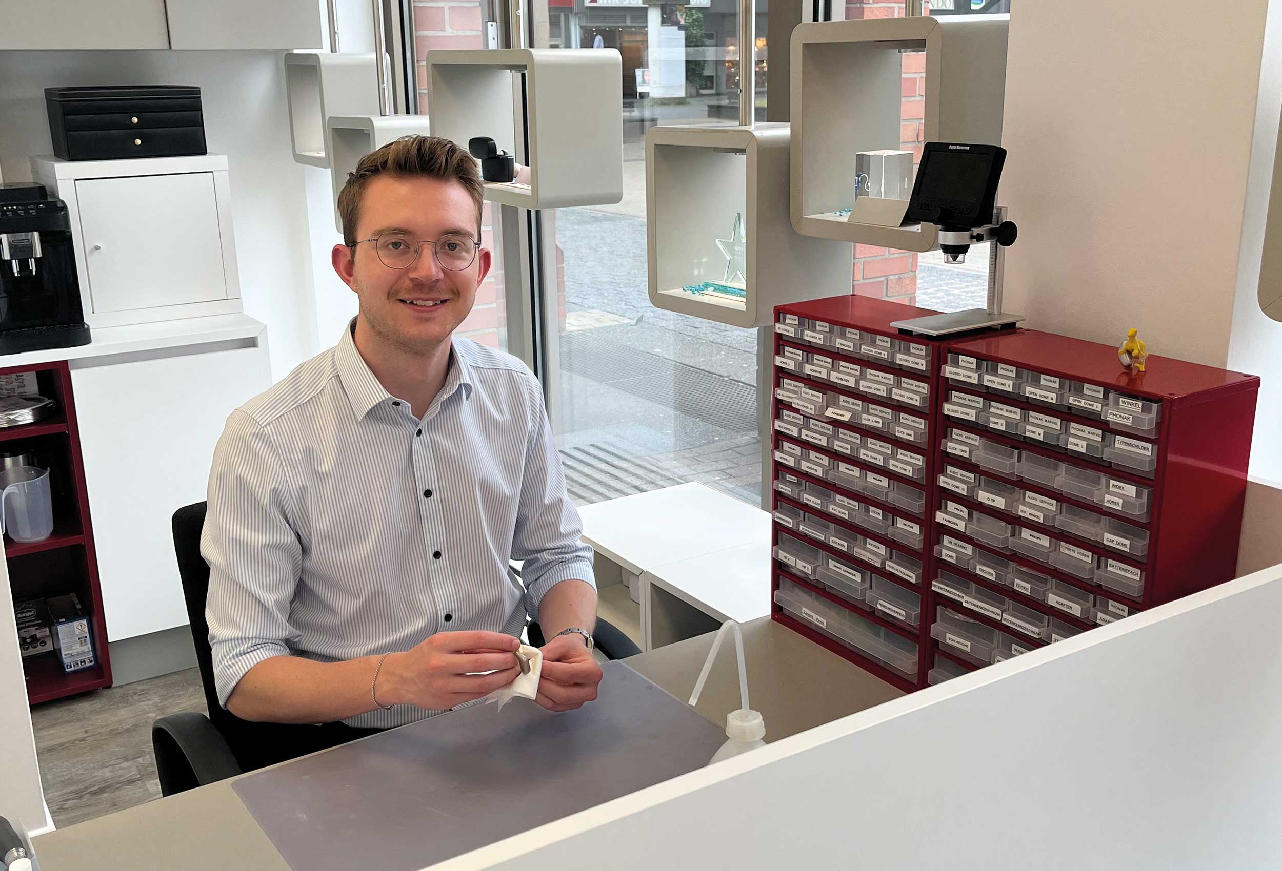 Mitarbeiter sitzt in der Werkstatt und reinigt ein Hörgerät